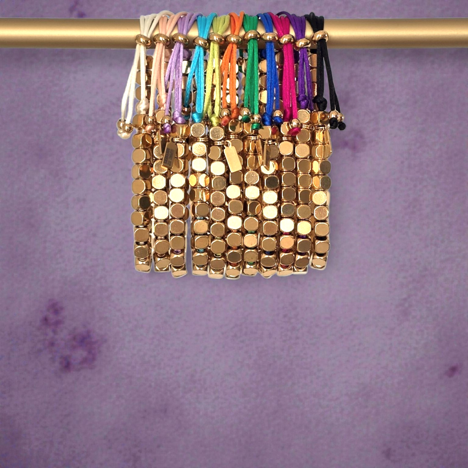 Gold beaded bracelets on a gold bar against a purple background