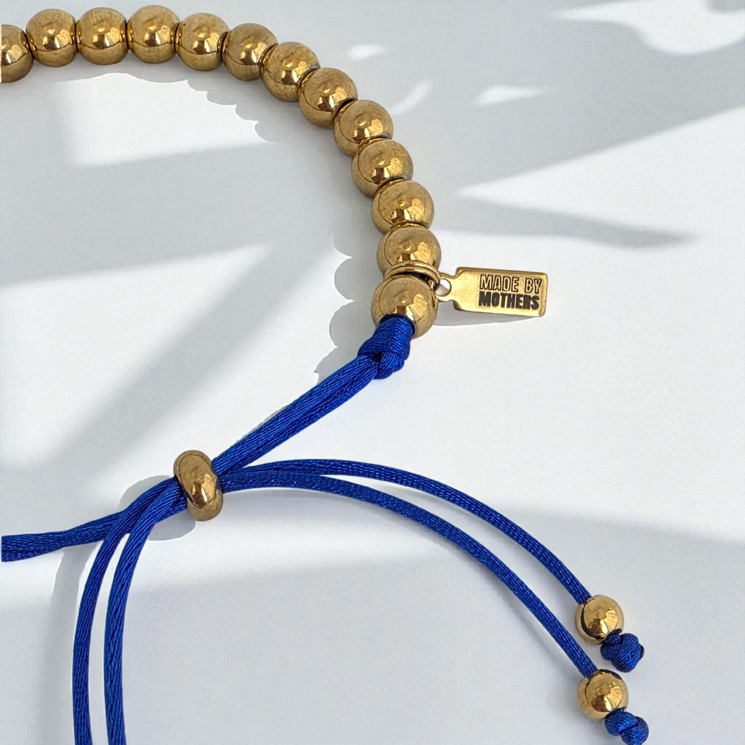 Bracelet with gold beads and blue cord on a white background