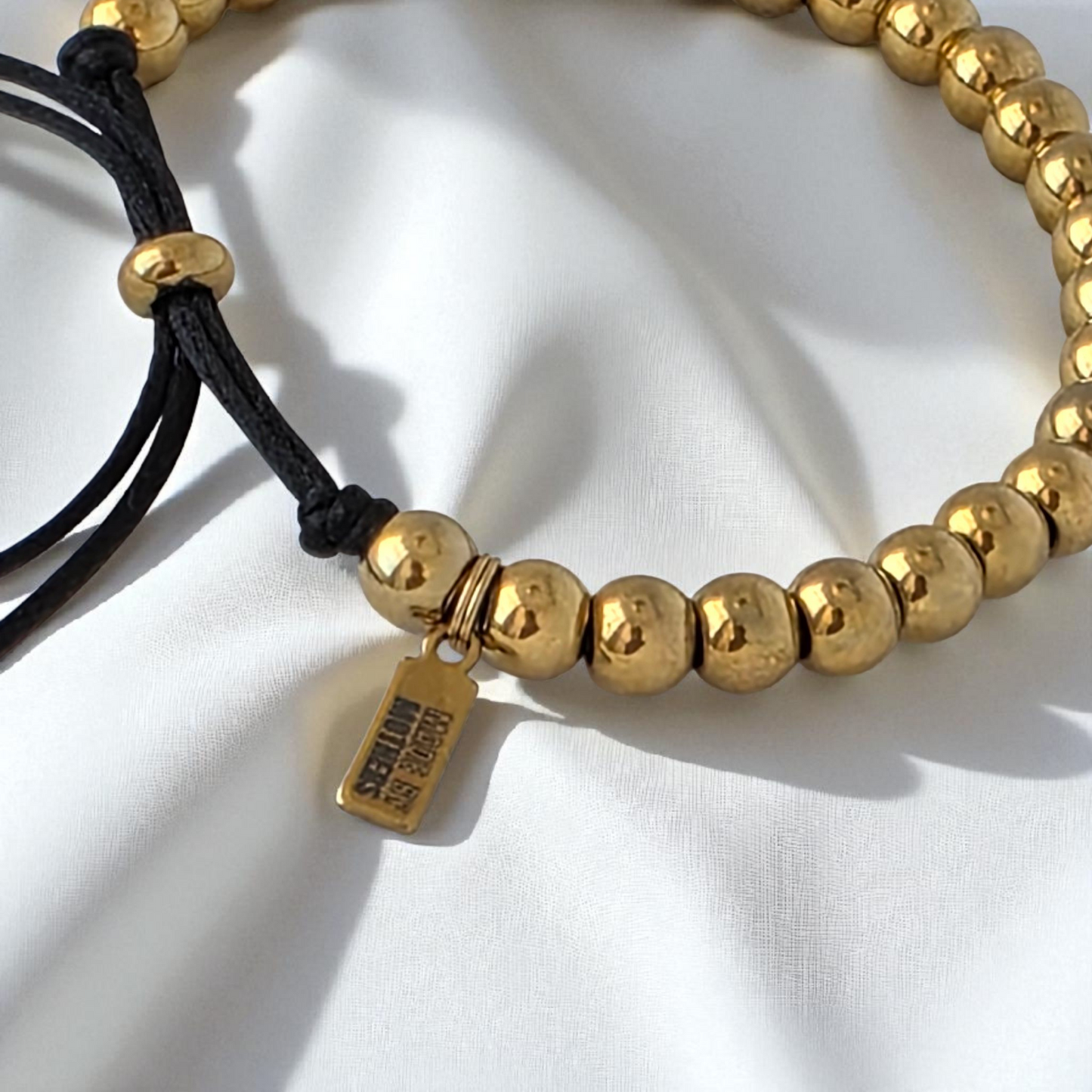 Gold beaded bracelet with a tag on a white background