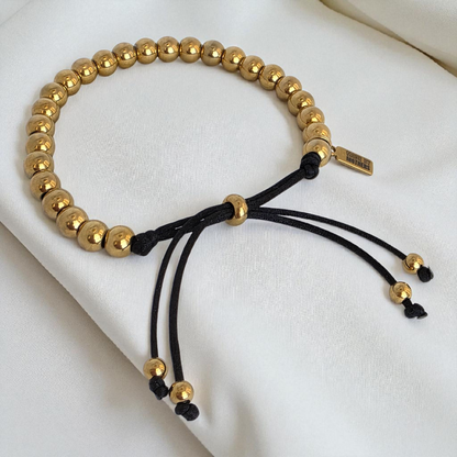 Gold beaded bracelet with black cord on a white surface