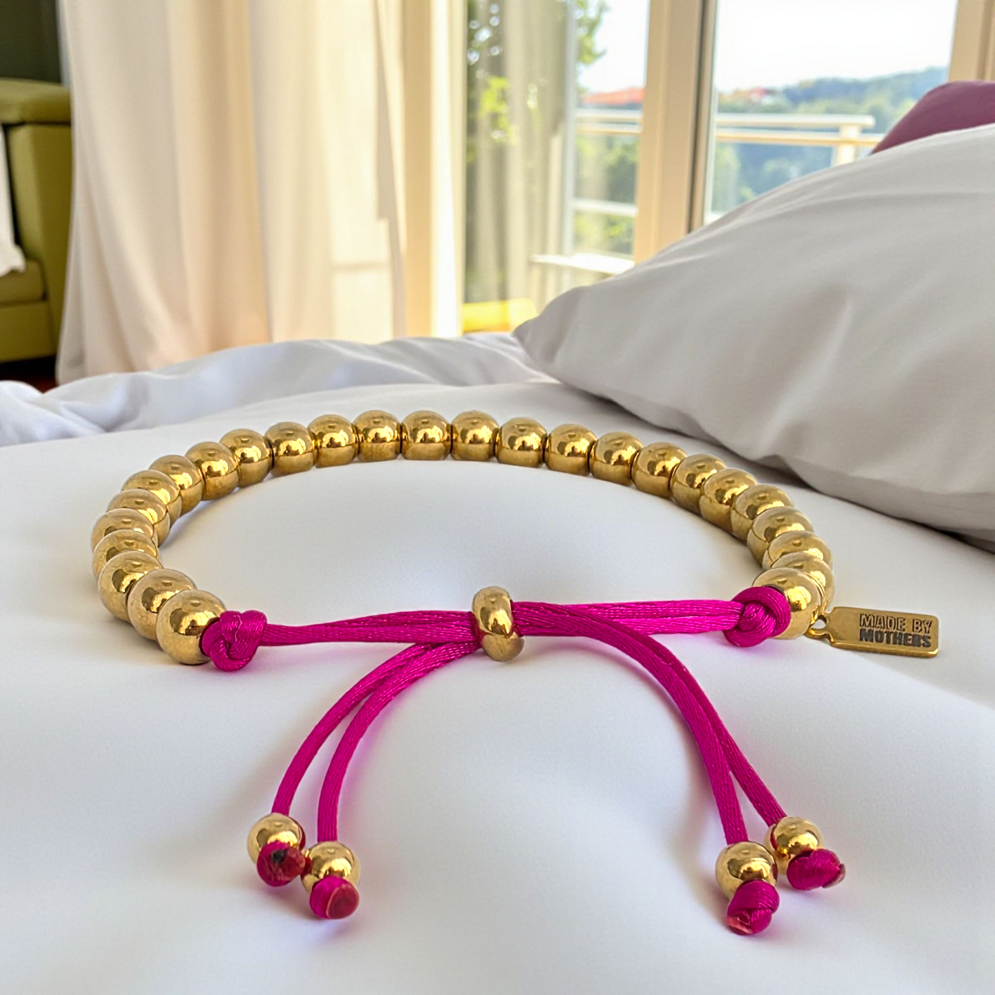Gold beaded bracelet with pink cord on a white surface, blurred background