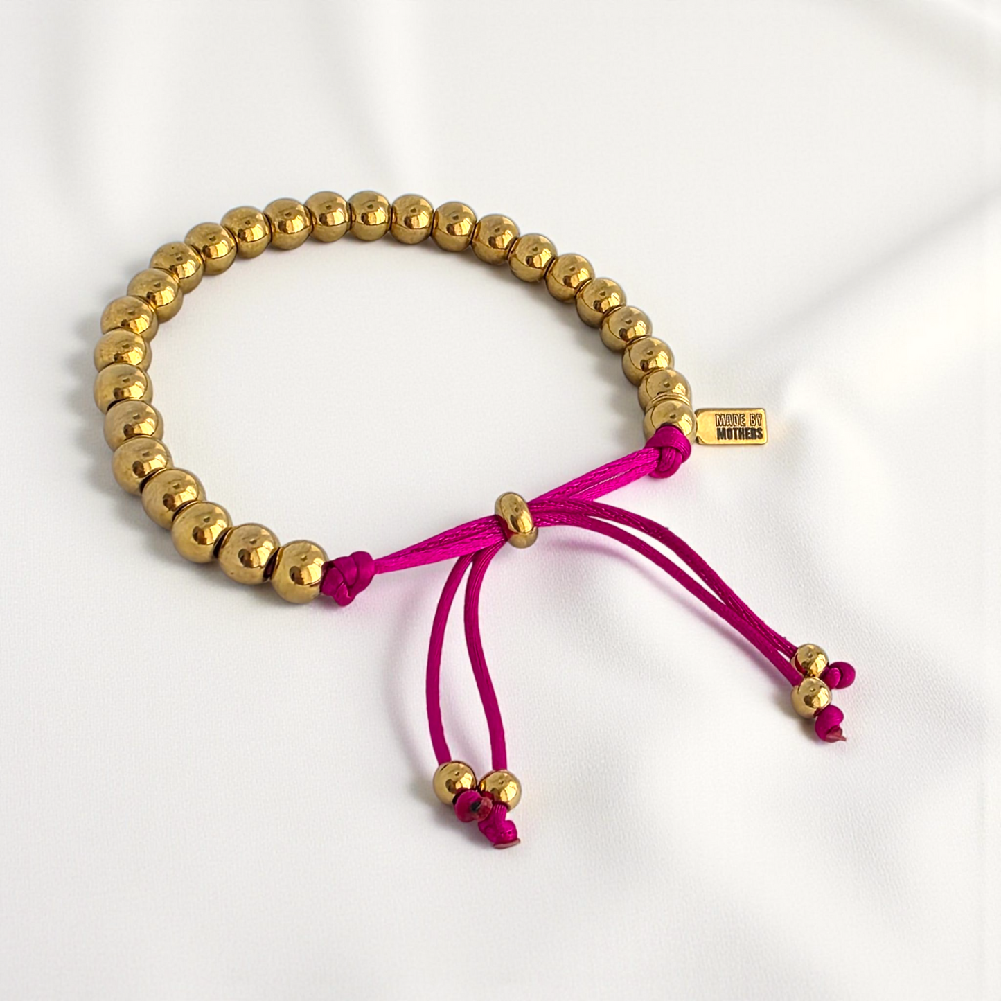 Gold beaded bracelet with pink cord on a white background