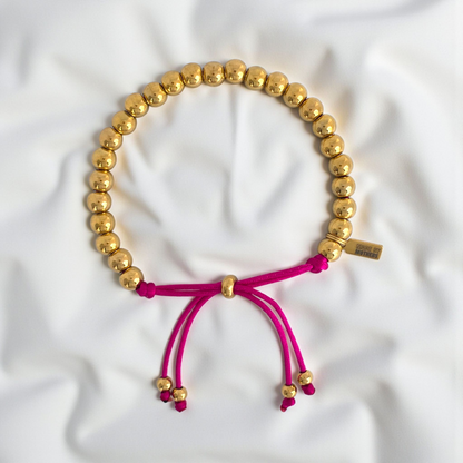 Gold beaded necklace with pink cord on a white fabric background