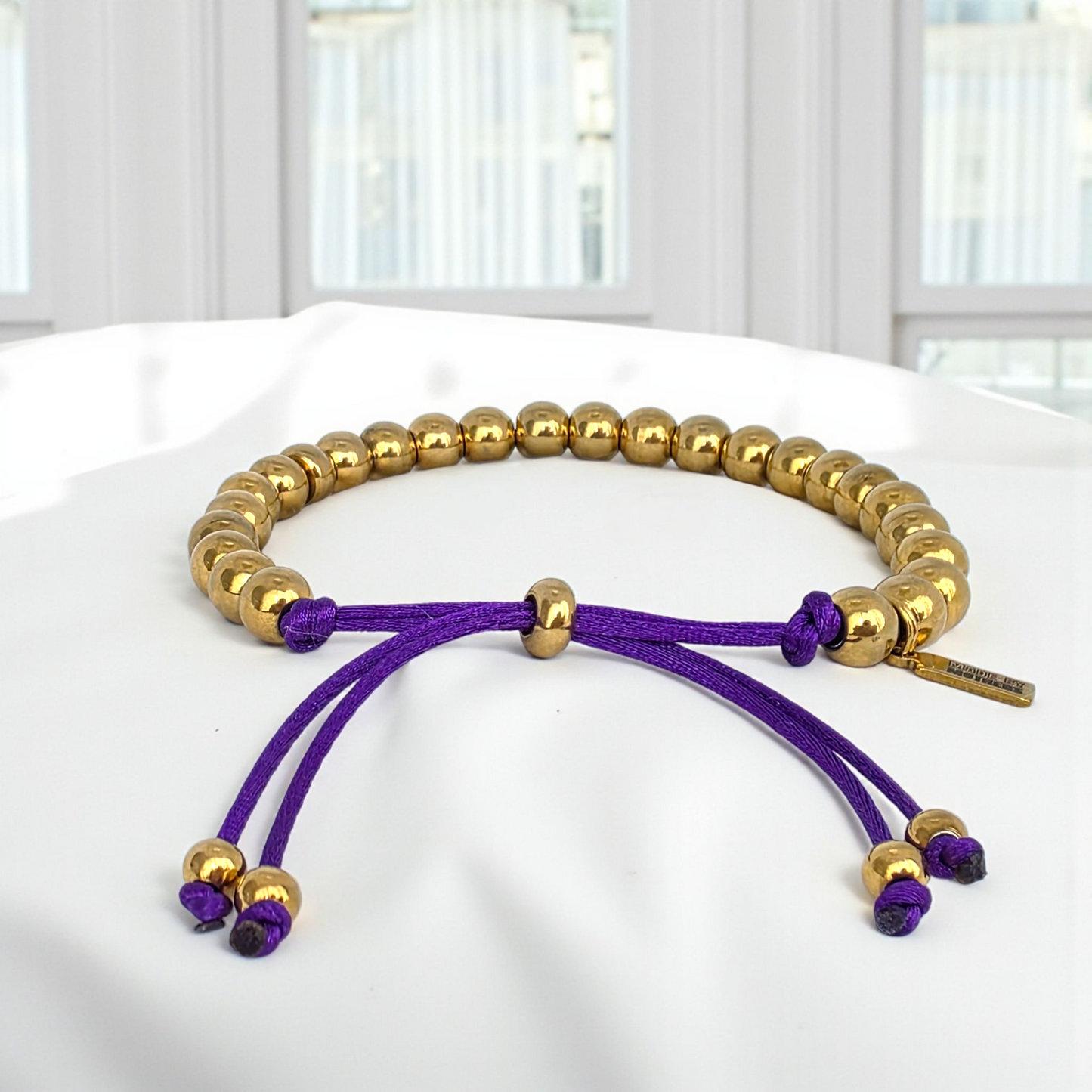 Gold and purple bracelet on a white surface with a blurred background