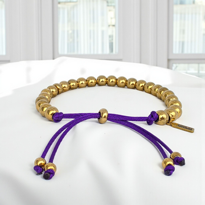Gold and purple bracelet on a white surface with a blurred background