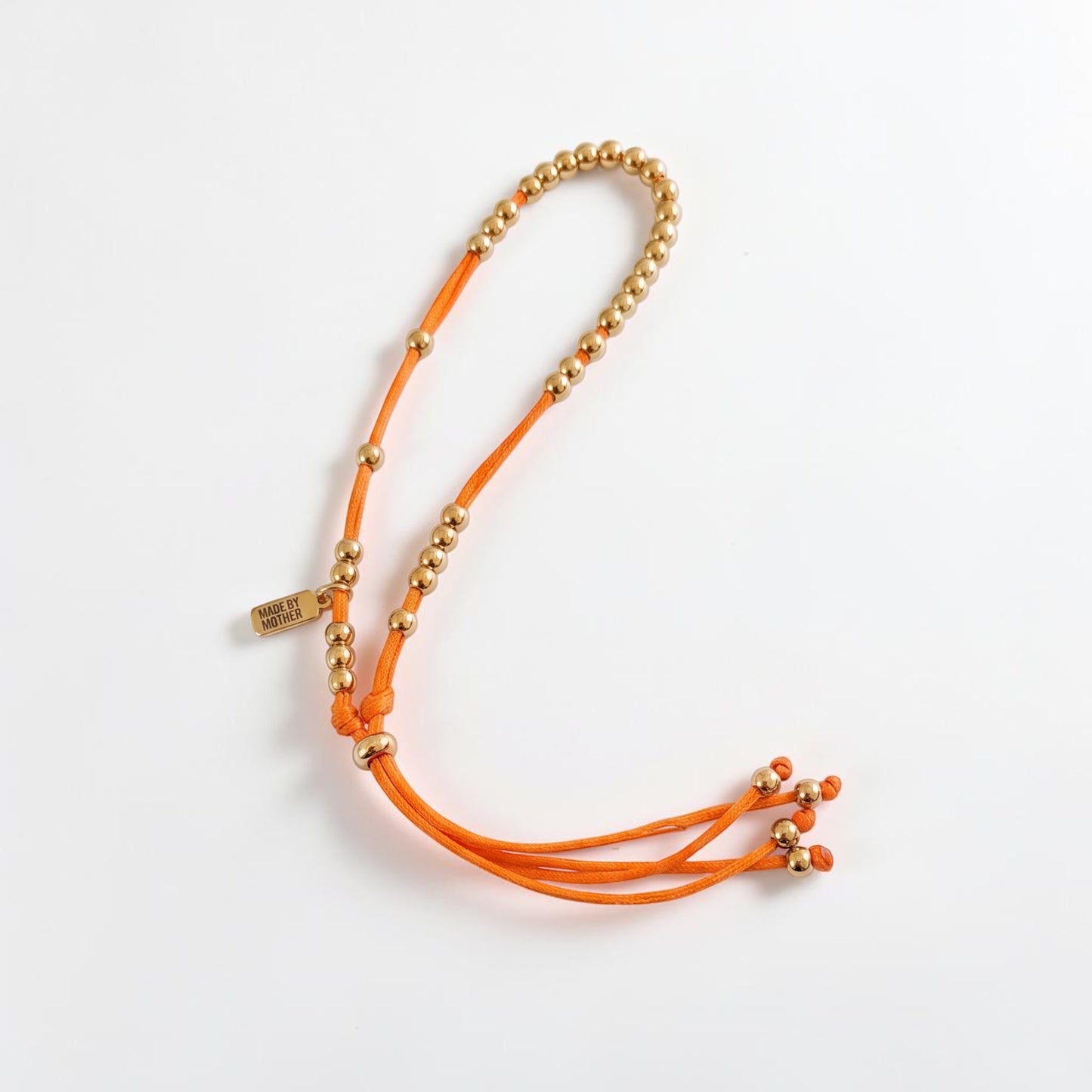 Made by Mothers The Luna Anklet featuring gold stainless steel beads on a vibrant orange silky satin cord.