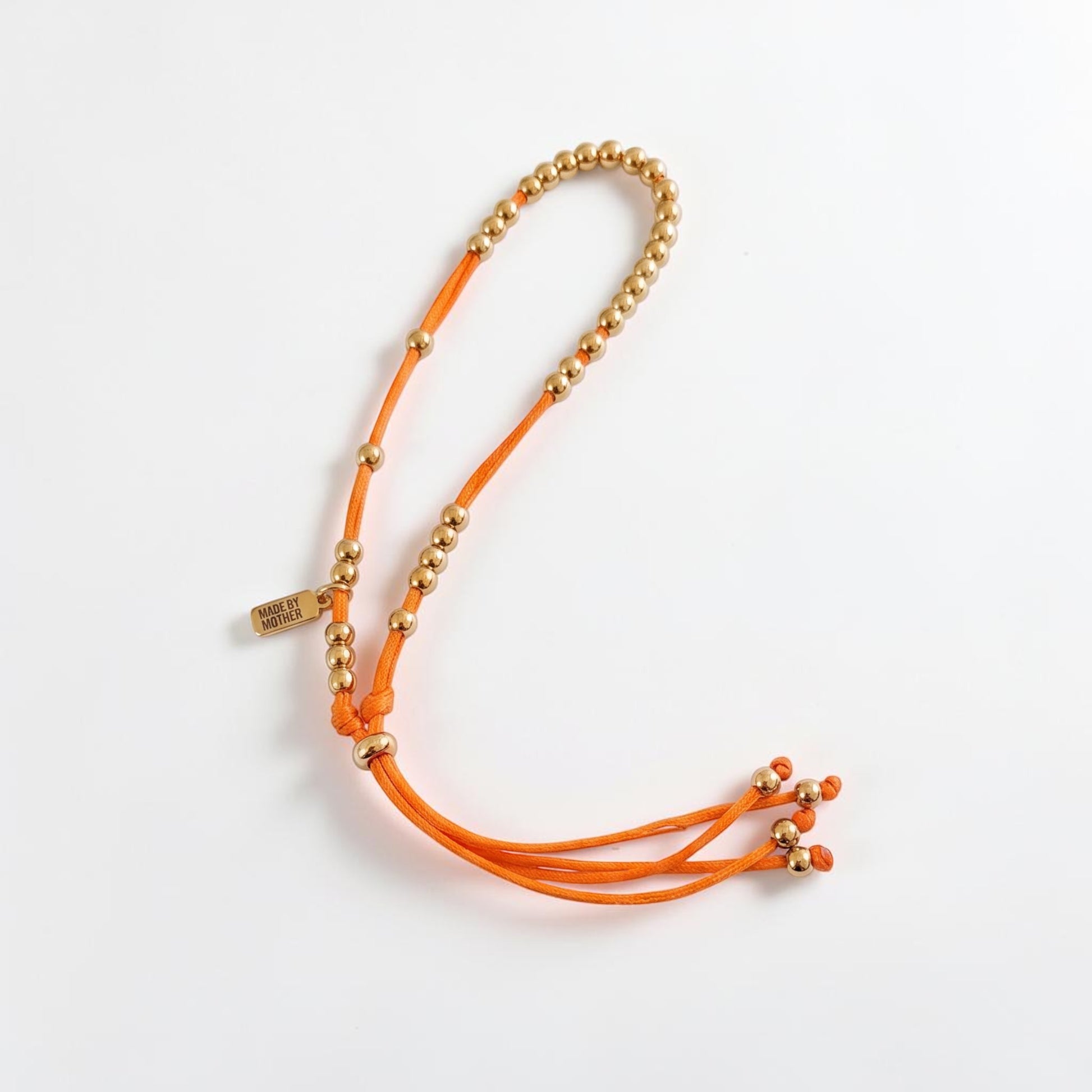 Made by Mothers The Luna Anklet featuring gold stainless steel beads on a vibrant orange silky satin cord.