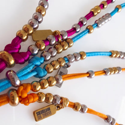 Made by Mothers Luna Anklets featuring vibrant satin cords and hypoallergenic stainless steel beads in gold and silver.