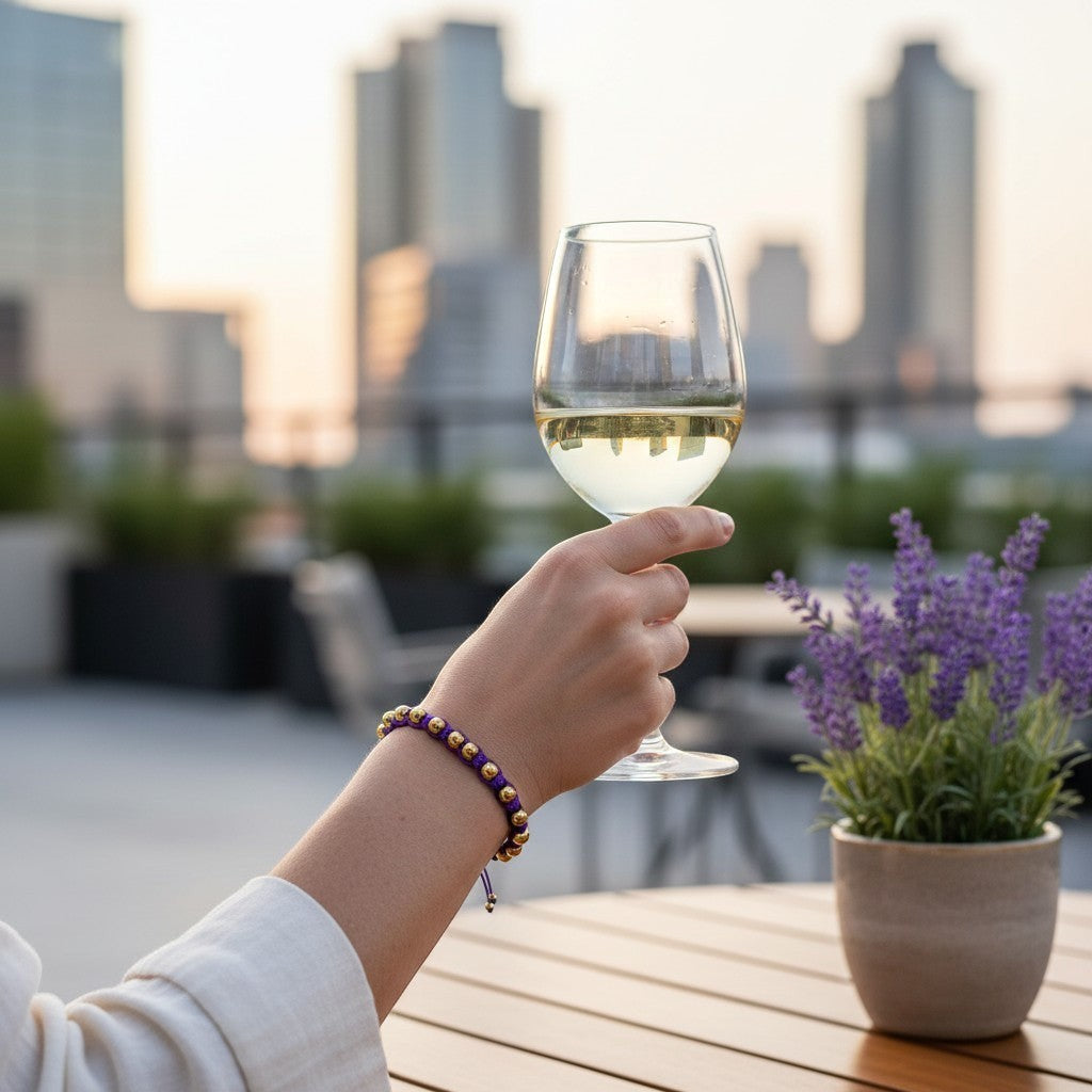 Made by Mothers Luna Aura bracelet with gold stainless steel beads on a purple satin cord, worn by a woman holding a glass of wine.