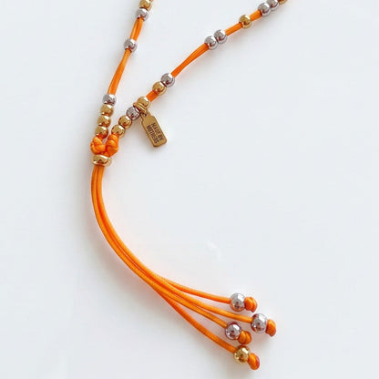 Made by Mothers Luna anklet featuring an orange satin cord with gold and silver stainless steel beads.