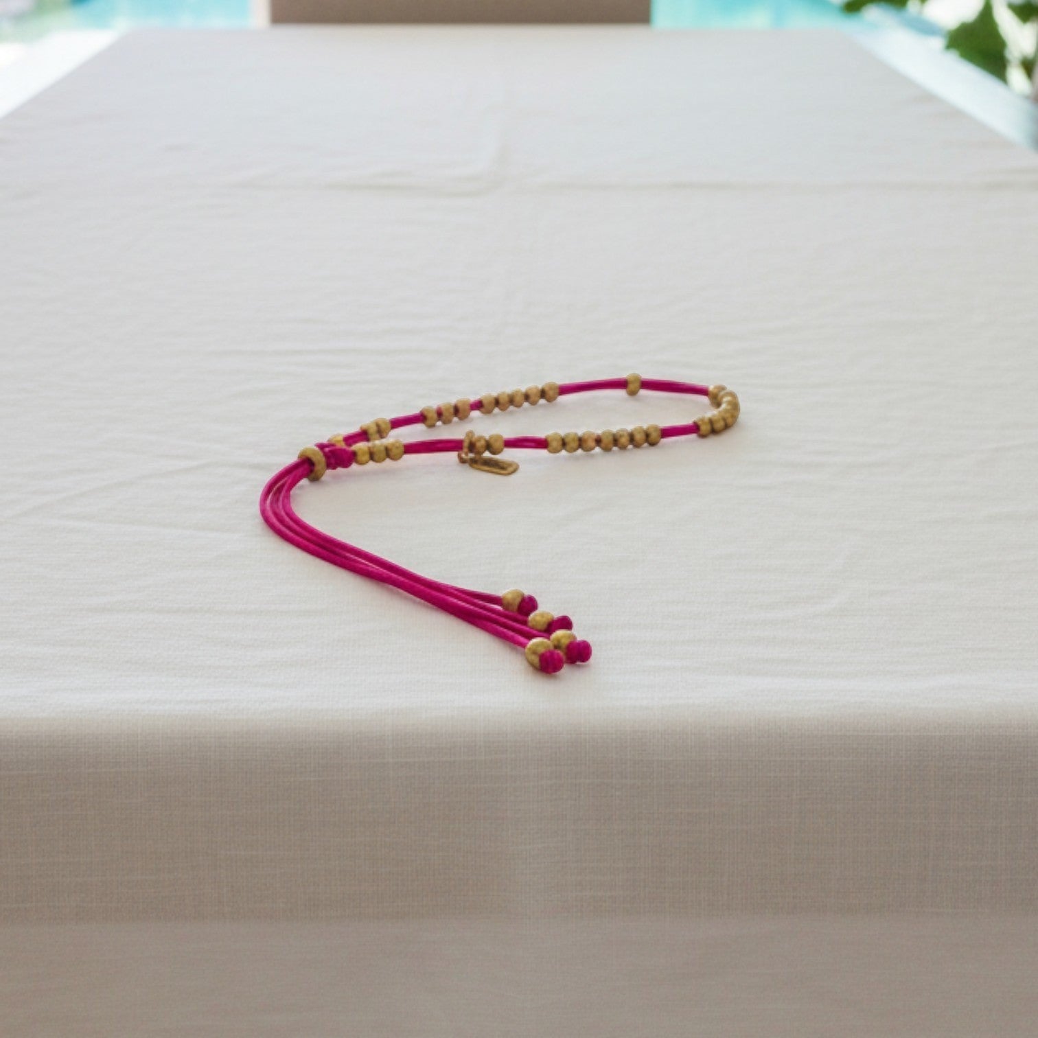 Made by Mothers Luna anklet with vibrant pink satin cord and hypoallergenic stainless steel beads on a white table.