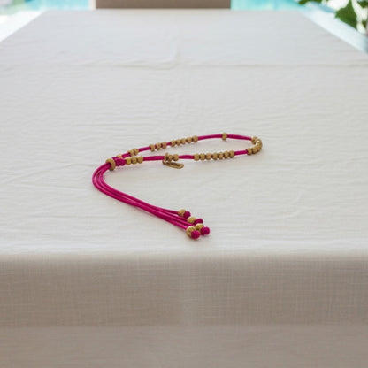Made by Mothers Luna anklet with vibrant pink satin cord and hypoallergenic stainless steel beads on a white table.