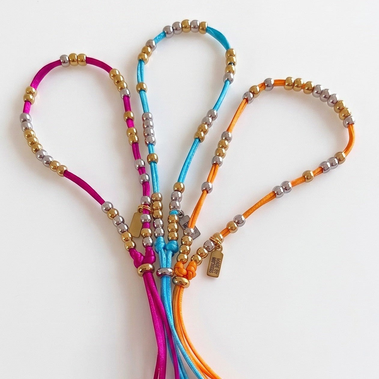 Made by Mothers Luna anklets in pink, blue, and orange satin cord with hypoallergenic stainless steel beads
